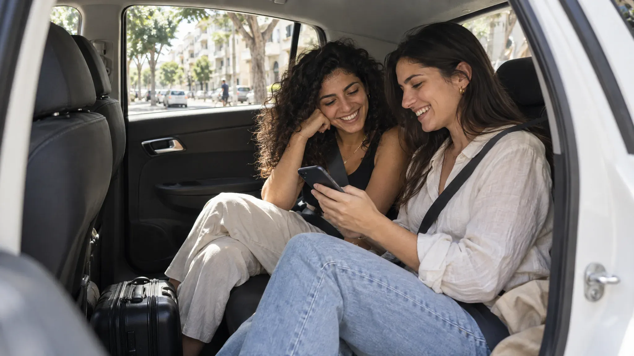 2 women laughing in the back seat of a car, looking at a phone together